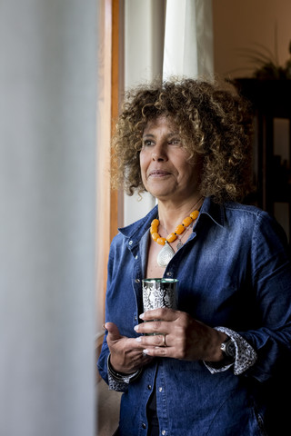 Frau hält ein Glas Tee und schaut aus dem Fenster, lizenzfreies Stockfoto