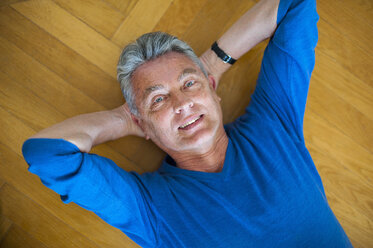 Portrait of smiling senior man lying on parquet floor - DIGF000495