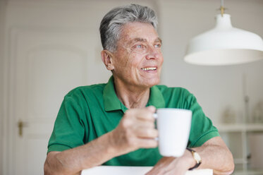Lächelnder älterer Mann zu Hause mit einer Tasse Kaffee in der Hand - DIGF000500