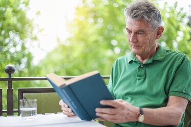 Älterer Mann sitzt auf dem Balkon und liest ein Buch - DIGF000517