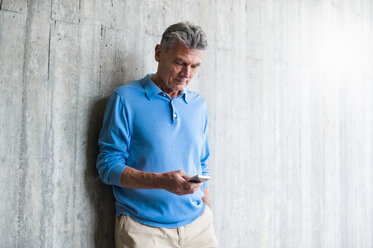Senior man at concrete wall looking on cell phone - DIGF000558