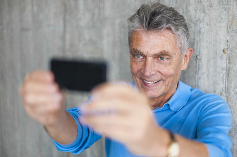 Lächelnder älterer Mann an einer Betonwand, der ein Selfie macht, lizenzfreies Stockfoto