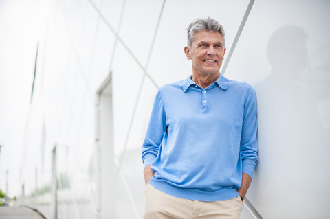 Smiling senior man leaning against a building stock photo