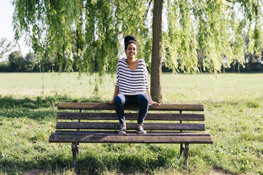 Porträt einer jungen Frau, die auf der Rückenlehne einer Parkbank sitzt - GIOF001092