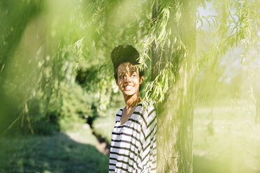 Portrait of young woman leaning against tree trunk - GIOF001093