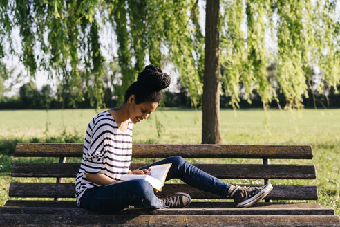 Junge Frau sitzt auf einer Parkbank und liest ein Buch - GIOF001097