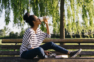 Junge Frau sitzt auf einer Parkbank und trinkt Kaffee zum Mitnehmen - GIOF001099
