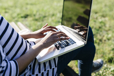 Woman sitting on park bench using laptop, close-up - GIOF001103