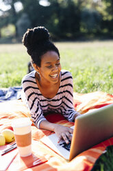 Laughing woman lying on blanket on a meadow using laptop - GIOF001109