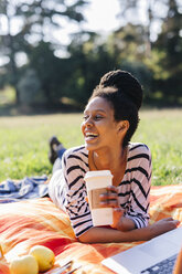 Glückliche Frau mit Kaffee zum Mitnehmen auf einer Decke auf einer Wiese liegend - GIOF001110