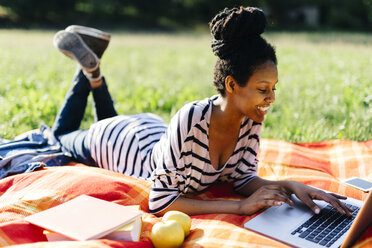 Young woman lying on blanket on a meadow using laptop - GIOF001111