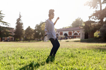 Woman dancing on a meadow while hearing music with earphones - GIOF001124