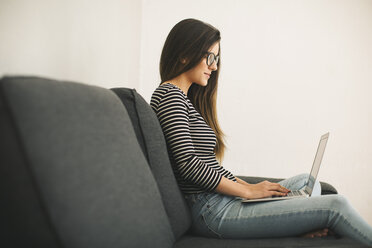 Junge Frau sitzt auf einer Couch und benutzt einen Laptop - EBSF001413