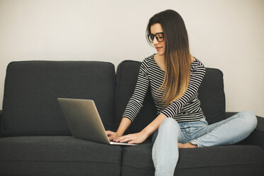 Young woman sitting on couch using laptop - EBSF001414