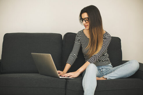 Junge Frau sitzt auf einer Couch und benutzt einen Laptop - EBSF001414