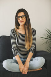 Young woman sitting cross-legged on couch - EBSF001415