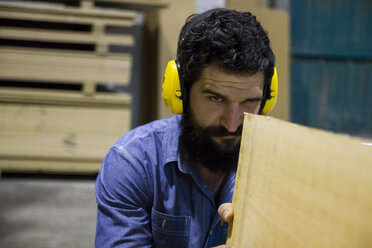 Craftsman with hearing protection examining a wooden plank - ABZF000551