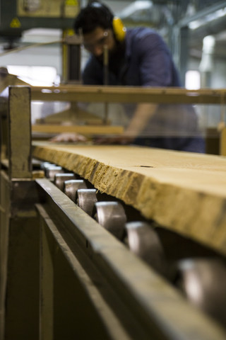 Handwerker mit Gehörschutz, Handschuhen und Schutzbrille bei der Arbeit mit einer Industriekreissäge in einer Fabrik, lizenzfreies Stockfoto