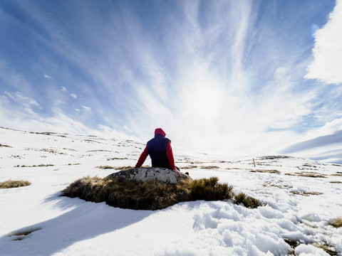 Spanien, Sierra de Gredos, Wanderer sitzt auf einem Felsen im Schnee, lizenzfreies Stockfoto