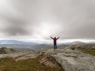 Spain, Sierra de Gredos, hiker standing with raised arms in mountains - LAF001638