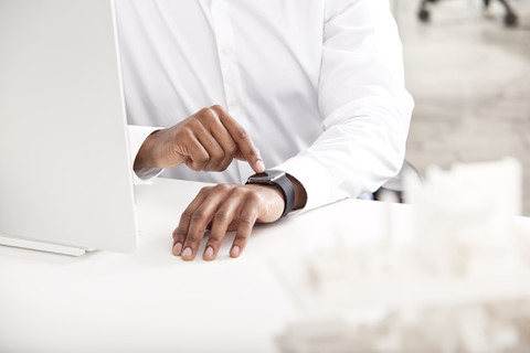 Männerhand stellt Smartwatch am Schreibtisch ein, lizenzfreies Stockfoto