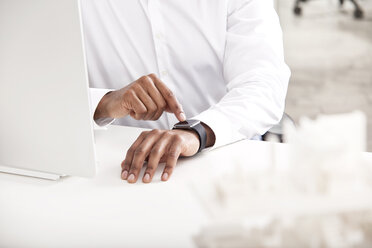 Männerhand stellt Smartwatch am Schreibtisch ein - MFRF000620