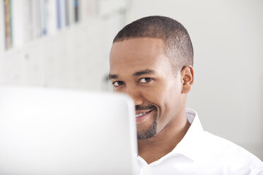 Porträt eines lächelnden Mannes hinter seinem Computer - MFRF000633