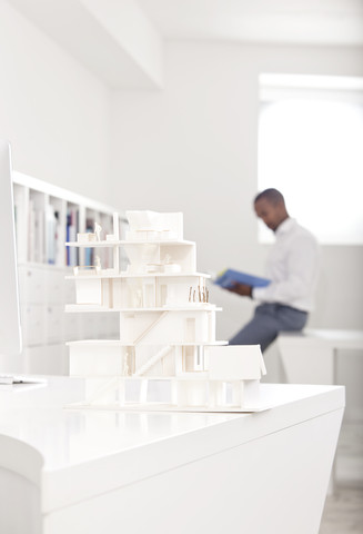 Architekturmodell auf einem Schreibtisch in einem Büro mit einem lesenden Mann im Hintergrund, lizenzfreies Stockfoto