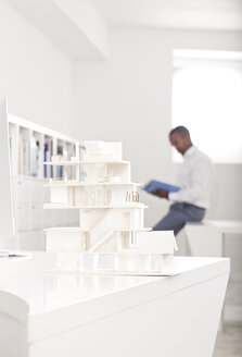 Architekturmodell auf einem Schreibtisch in einem Büro mit einem lesenden Mann im Hintergrund - MFRF000643