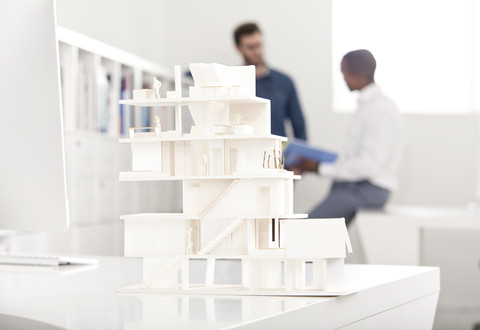 Architekturmodell auf einem Schreibtisch in einem Büro mit zwei sprechenden Personen im Hintergrund, lizenzfreies Stockfoto