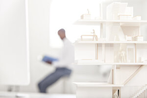 Architekturmodell auf einem Schreibtisch in einem Büro mit einem lesenden Mann im Hintergrund - MFRF000647