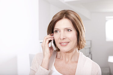 Porträt einer lächelnden Frau, die mit einem Smartphone im Büro telefoniert - MFRF000670