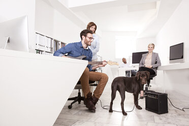 Vier Kollegen, die eine Pause im Büro machen und einen Hund betrachten - MFRF000695
