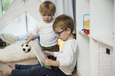 Two little boys playing at home, looking at picture book - LFOF000233