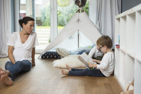 Mutter sitzt mit ihren Söhnen auf dem Boden und liest ein Kinderbuch, lizenzfreies Stockfoto