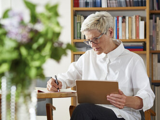 Senior woman with digital tablet writing down something - DISF002488