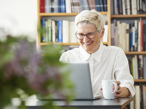 Porträt einer lachenden älteren Frau, die zu Hause ein digitales Tablet benutzt, lizenzfreies Stockfoto