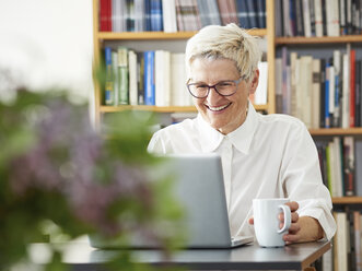 Porträt einer lachenden älteren Frau, die zu Hause ein digitales Tablet benutzt - DISF002490