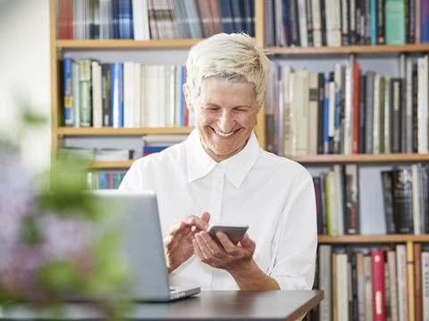 Porträt einer lächelnden älteren Frau mit digitalem Tablet und Smartphone zu Hause, lizenzfreies Stockfoto