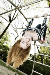 Portrait of smiling girl hanging upside down on jungle gym - JATF000862