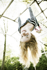 Portrait of smiling girl hanging upside down on jungle gym - JATF000863