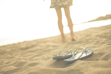 Spanien, Teneriffa, junge Frau am Strand stehend, Flip-Flops im Vordergrund - SIPF000514