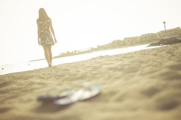 Spanien, Teneriffa, junge Frau am Strand stehend, Flip-Flops im Vordergrund - SIPF000515