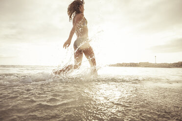 Spain, Tenerifa, young woman running into water against the sun - SIPF000521