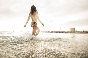 Spain, Tenerifa, young woman running into water against the sun - SIPF000522