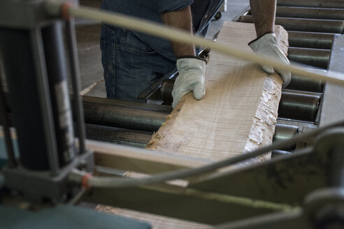 Man with gloves putting a wood plank on an industrial circular saw in a factory - ABZF000597