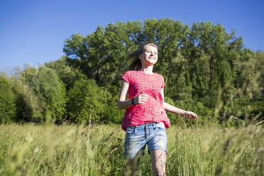 Glückliches Teenager-Mädchen läuft auf einer Wiese - MRAF000051