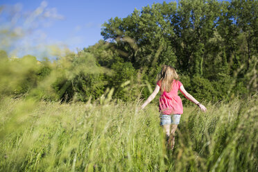 Back view of teenage girl walking on a meadow - MRAF000052