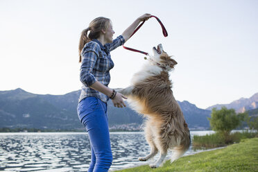 Italien, Lecco, junges Mädchen spielt mit ihrem Hund am Seeufer - MRAF000064