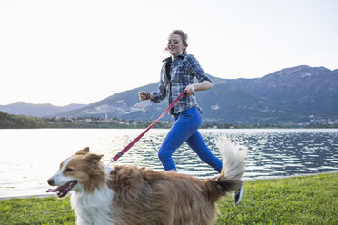Italien, Lecco, junges Mädchen läuft mit ihrem Hund am Seeufer - MRAF000065